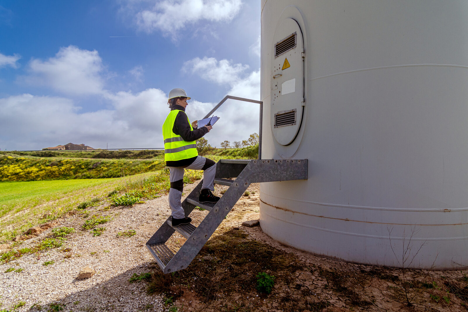 A wind-turbine technician in safety gear climbing a turbine